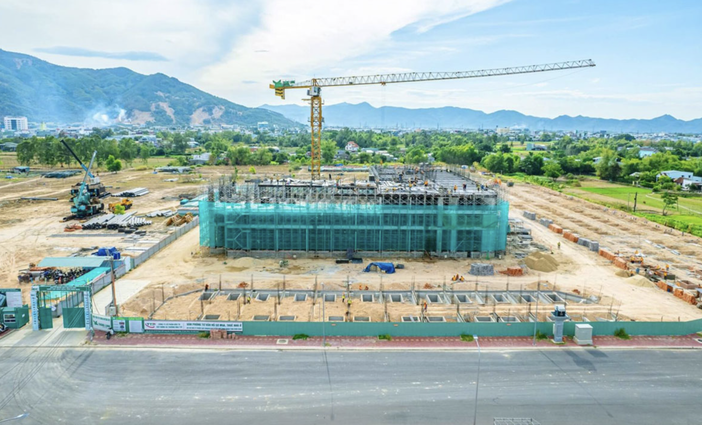 Công trường xây dựng khu nhà cao tầng với cần cẩu, nền móng và công nhân vận động dưới bầu trời xanh.