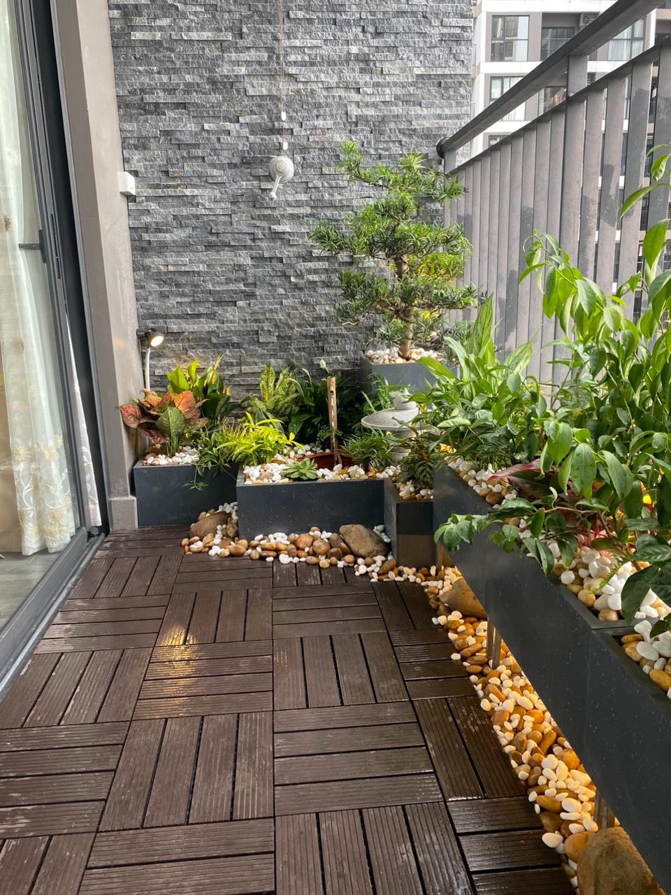Ban công lát gỗ trang trí cây xanh và sỏi, tạo không gian thư giãn phong cách hiện đại.