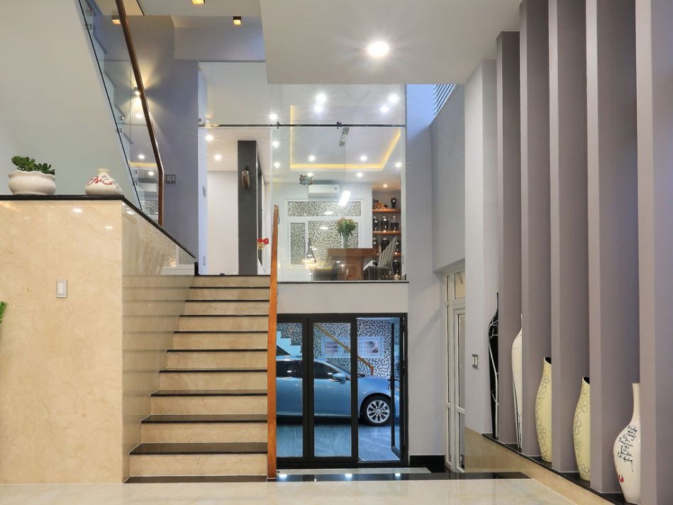 Ngôi nhà hiện đại với cầu thang gỗ, sàn đá hoa cương, cửa kính và trang trí bình hoa nghệ thuật.