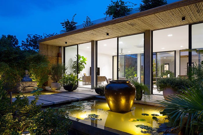 Nhà hiện đại với sân vườn và hồ nước, nội thất kính sáng đèn, không gian xanh thư giãn buổi tối.