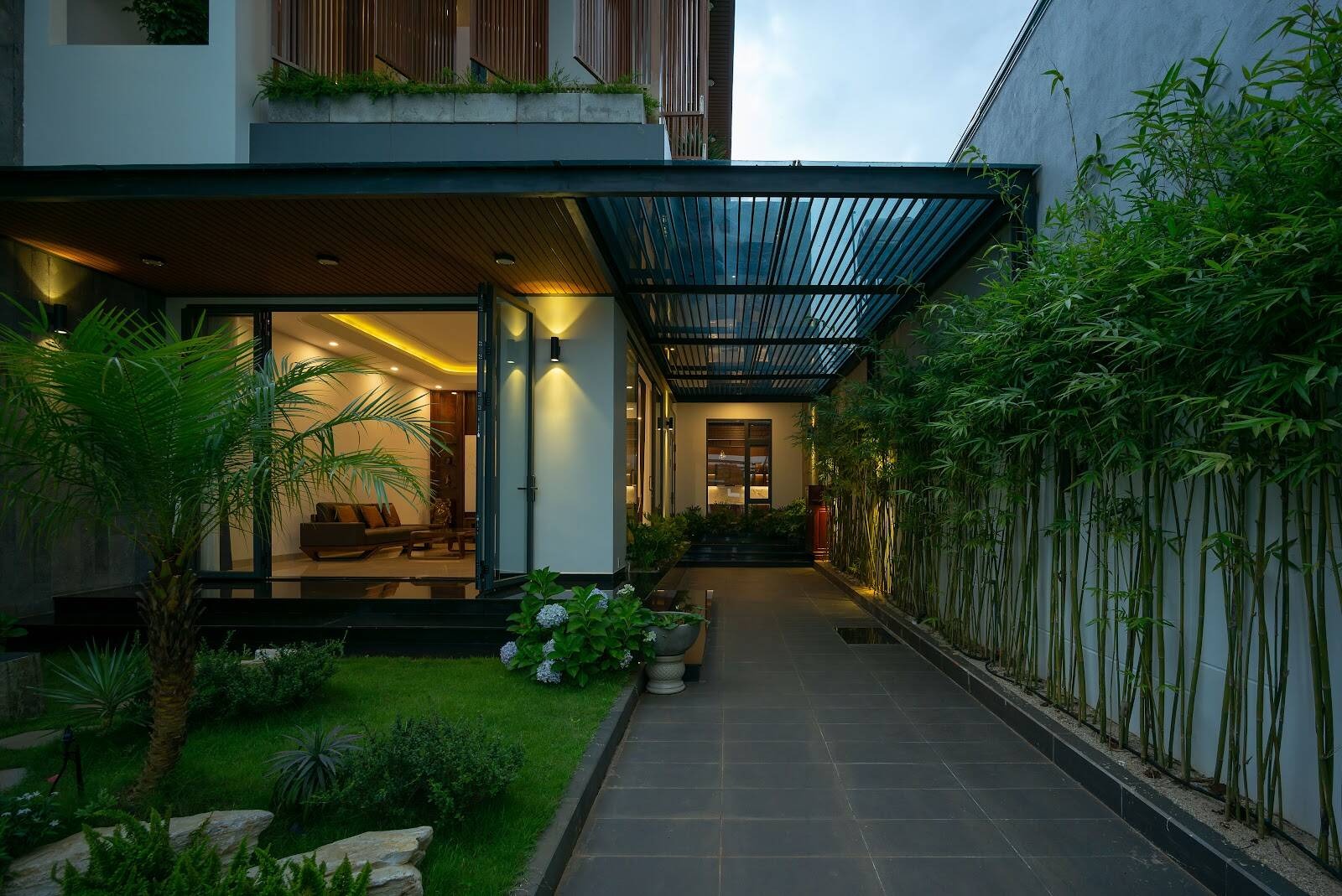 Ngôi nhà hiện đại với vườn cây xanh, ánh sáng ban đêm và nội thất thoáng đãng, tạo không gian sống tiện nghi.