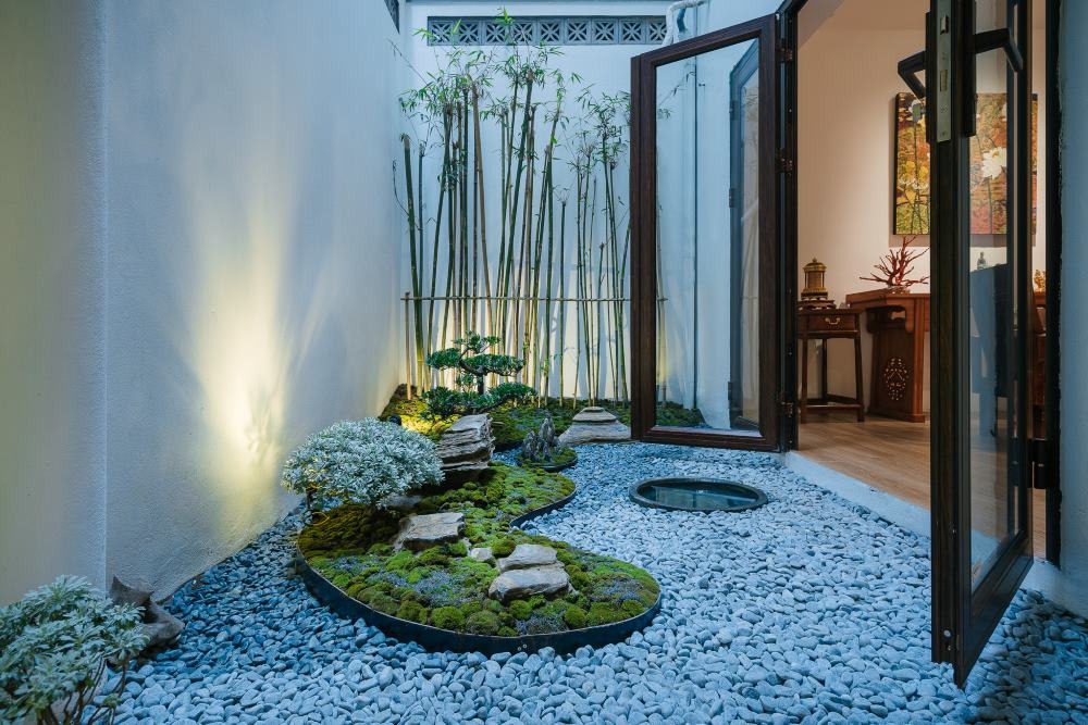 Sân vườn nhỏ với cây tre, đá và cỏ xanh, cửa kính mở hướng vào nội thất nhà.
