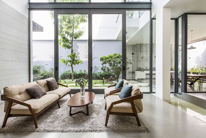 Phòng khách hiện đại với cửa kính lớn, sofa màu be, bàn gỗ, cây xanh ngoài trời.