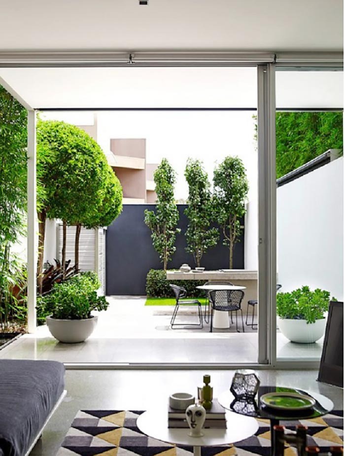 Phòng khách hiện đại với cửa kính trượt nhìn ra sân vườn xanh mát và bàn ăn ngoài trời.