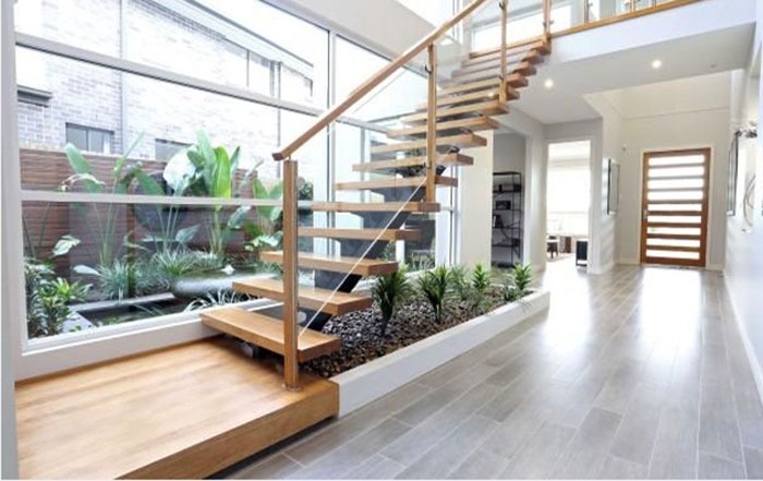 Cầu thang gỗ hiện đại trong không gian nội thất với cây xanh và cửa sổ lớn, ánh sáng tự nhiên tràn ngập.
