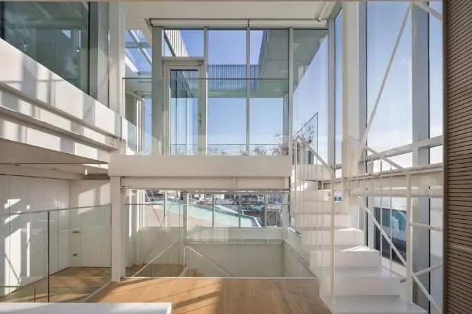 Ngôi nhà kính hiện đại với cầu thang trắng và sàn gỗ, tầm nhìn ra ngoài trời sáng rực.