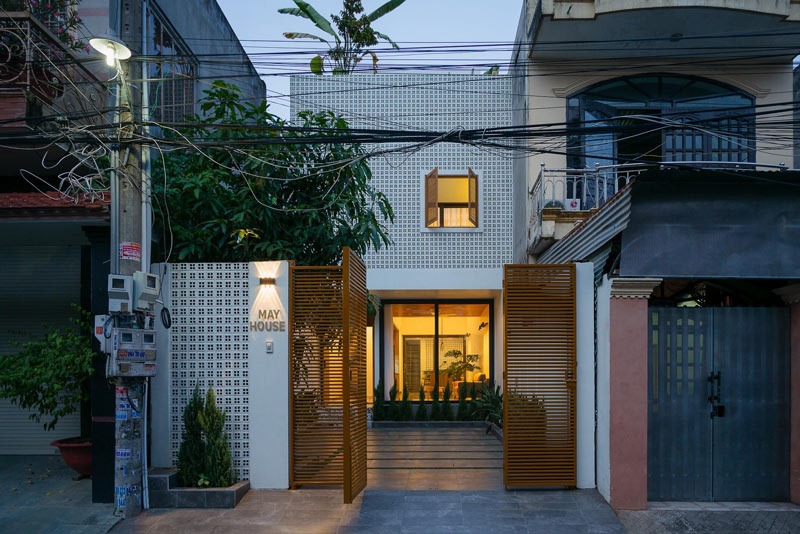 Mặt tiền nhà hiện đại với cửa mở và ánh sáng ấm áp buổi tối, thiết kế tối giản và cây xanh trang trí.