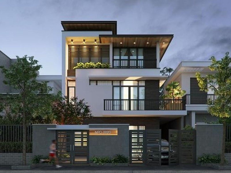 Biệt thự hiện đại với thiết kế ba tầng, ánh sáng buổi tối rực rỡ, cây xanh trang trí phía trước.