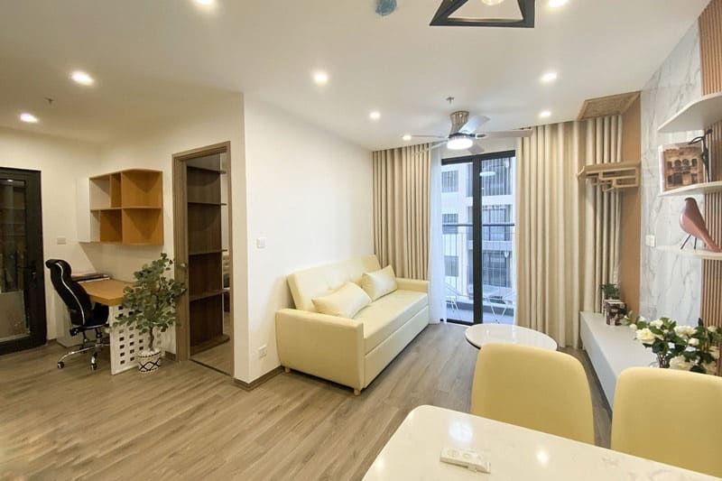 Phòng khách hiện đại với ghế sofa màu vàng nhạt, bàn làm việc và cửa sổ lớn nhìn ra cảnh quan bên ngoài.