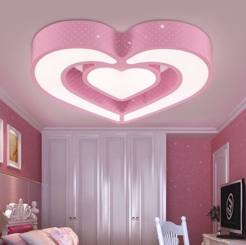 Đèn trần hình trái tim màu hồng trong phòng ngủ với nội thất màu hồng và tủ trắng.