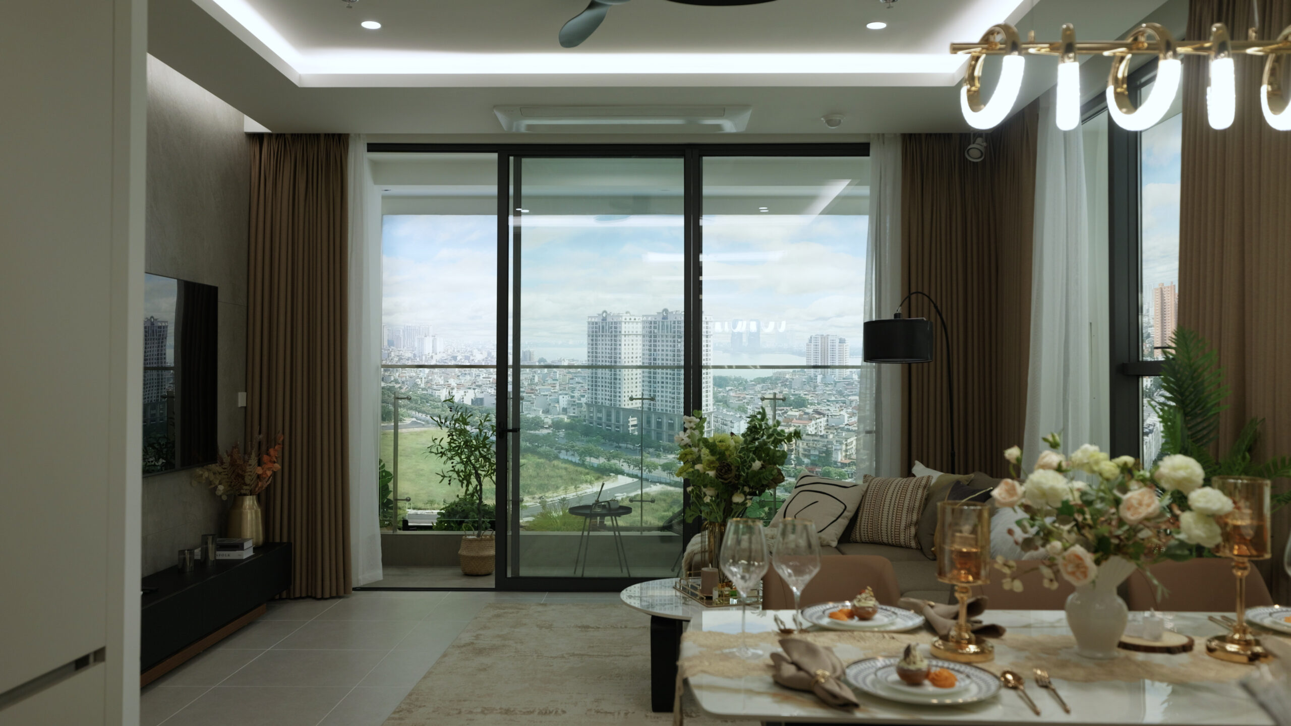 Phòng khách hiện đại với cửa kính lớn nhìn ra thành phố, nội thất sang trọng và trang trí hoa tươi.