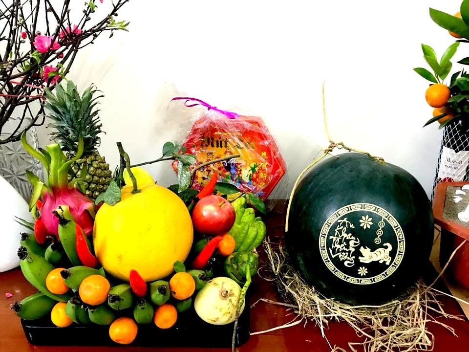 Trái cây Tết trên bàn, gồm dưa hấu khắc chữ, thanh long, quýt, ớt và chuối, trang trí cùng hoa đào.