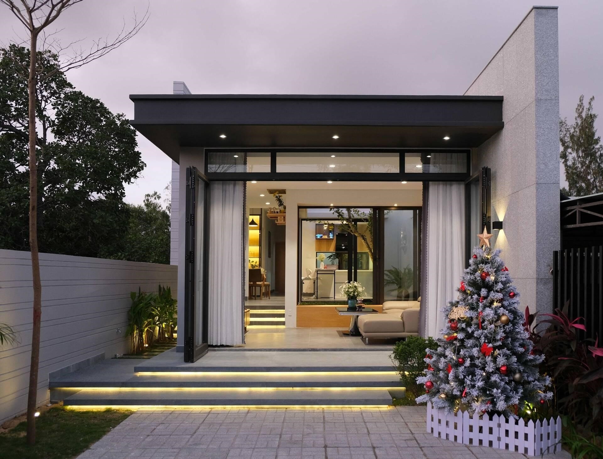Ngôi nhà hiện đại với cây thông Noel trang trí rực rỡ bên ngoài, lối vào rộng với đèn chiếu sáng.