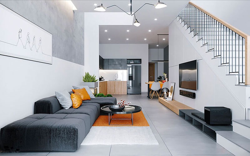 Phòng khách hiện đại với ghế sofa xám, bàn trà, tranh treo tường; không gian bếp liền kề, cầu thang tay vịn gỗ.