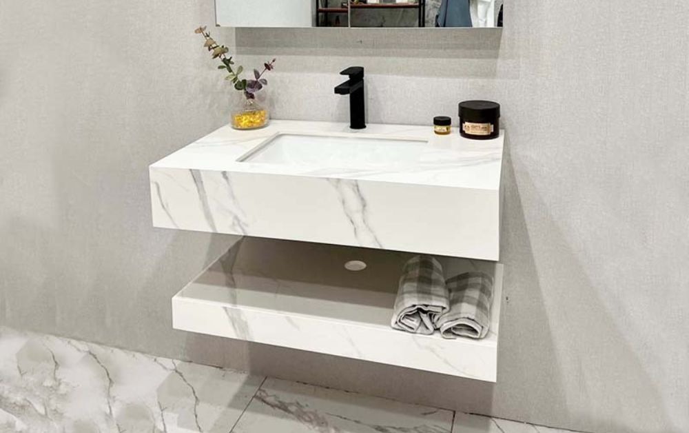 Bồn rửa mặt treo tường bằng đá cẩm thạch trắng với vòi đen và kệ để khăn trong phòng tắm hiện đại.
