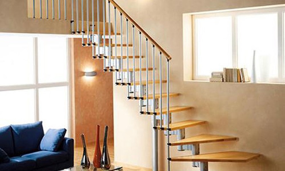 Cầu thang xoắn hiện đại bằng gỗ và kim loại trong phòng khách sáng sủa với sofa xanh và cửa sổ lớn.