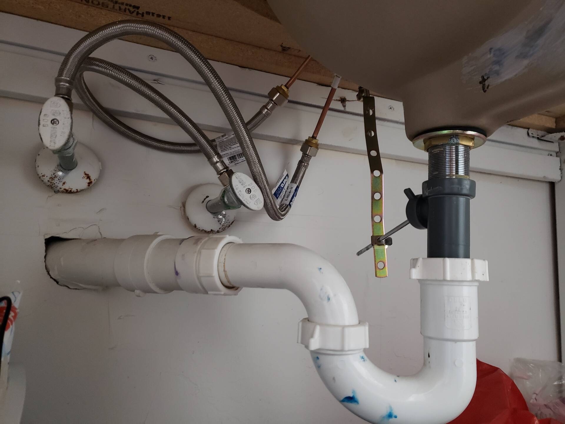 Hệ thống ống nước dưới bồn rửa, gồm ống nhựa PVC và dây dẫn bằng thép không gỉ.