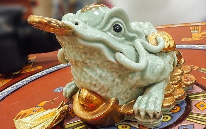 Tượng cóc ngậm tiền phong thủy, mang ý nghĩa may mắn và tài lộc, làm từ gốm sứ, đặt trên đĩa đỏ trang trí.