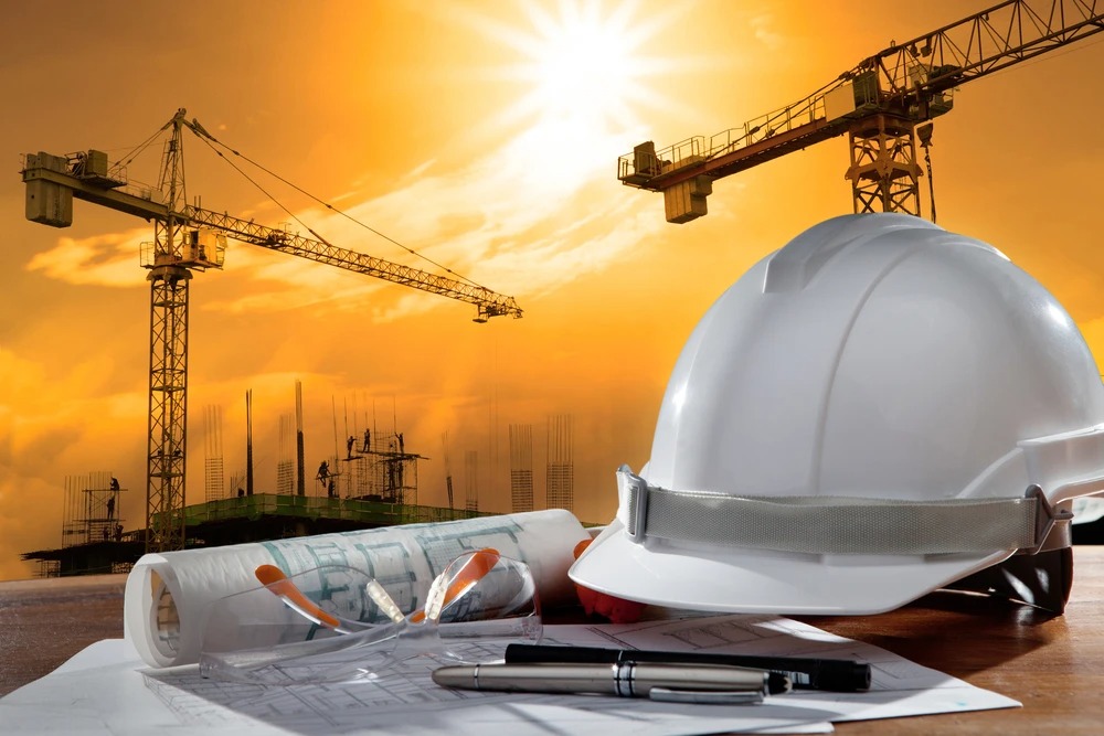 Nón bảo hộ công trình xây dựng với cần cẩu trong ánh hoàng hôn, đại diện cho ngành xây dựng.