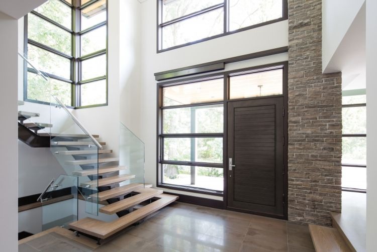 Lối vào hiện đại với cửa sổ rộng và cầu thang gỗ kính, ánh sáng tự nhiên tràn ngập không gian.