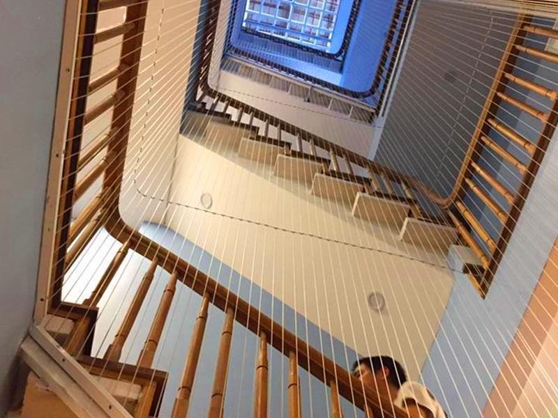 Cầu thang xoắn ốc hiện đại nhìn từ dưới lên, với lan can gỗ và dây cáp bảo vệ trong tòa nhà cao tầng.