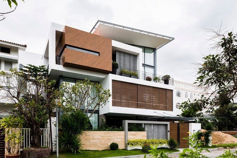Nhà hiện đại với thiết kế ba tầng, cửa kính và ban công cây xanh, tọa lạc giữa không gian thiên nhiên yên tĩnh.