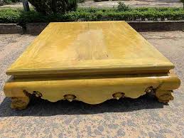 Phản gỗ lớn với mặt sáng bóng đặt trên nền gạch ngoài trời.