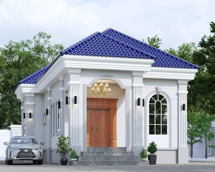 Nhà một tầng mái xanh, cửa gỗ lớn, cửa sổ vòm, cây cảnh trước nhà, xung quanh có cây xanh.