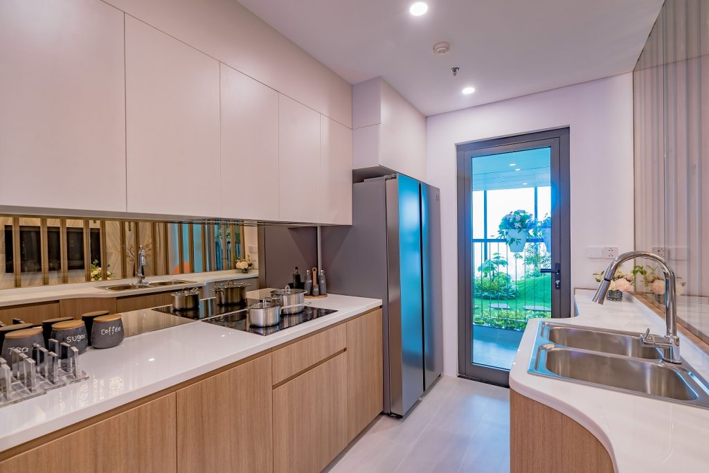 Nhà bếp hiện đại với tủ gỗ sáng, tủ lạnh inox và cửa sổ hướng ra khu vườn xanh.