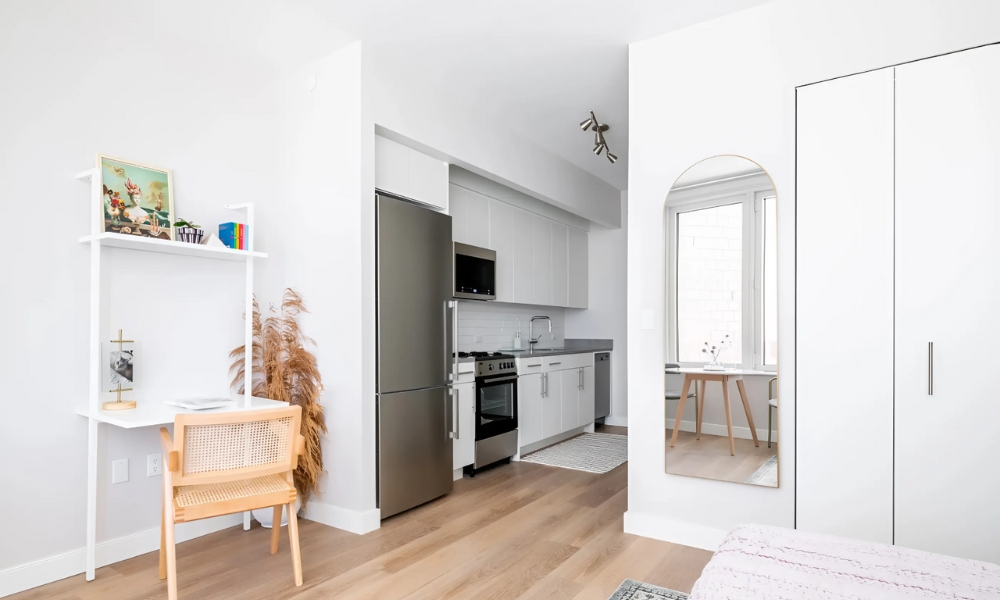 Phòng bếp hiện đại trong căn hộ nhỏ gọn với tủ lạnh, lò nướng và bàn ăn nhỏ cạnh cửa sổ.