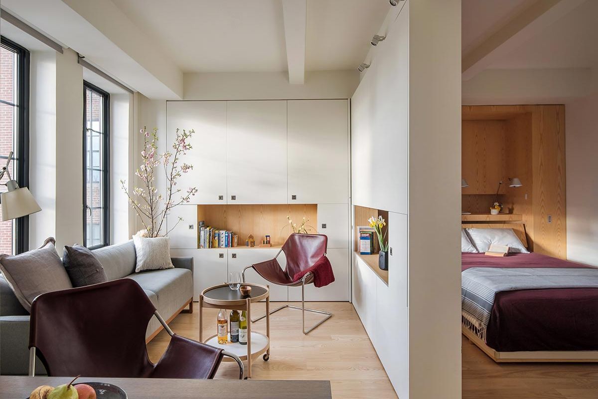 Phòng khách hiện đại với ghế đỏ nổi bật, sofa xám và cây hoa, gần kề với phòng ngủ gọn gàng.