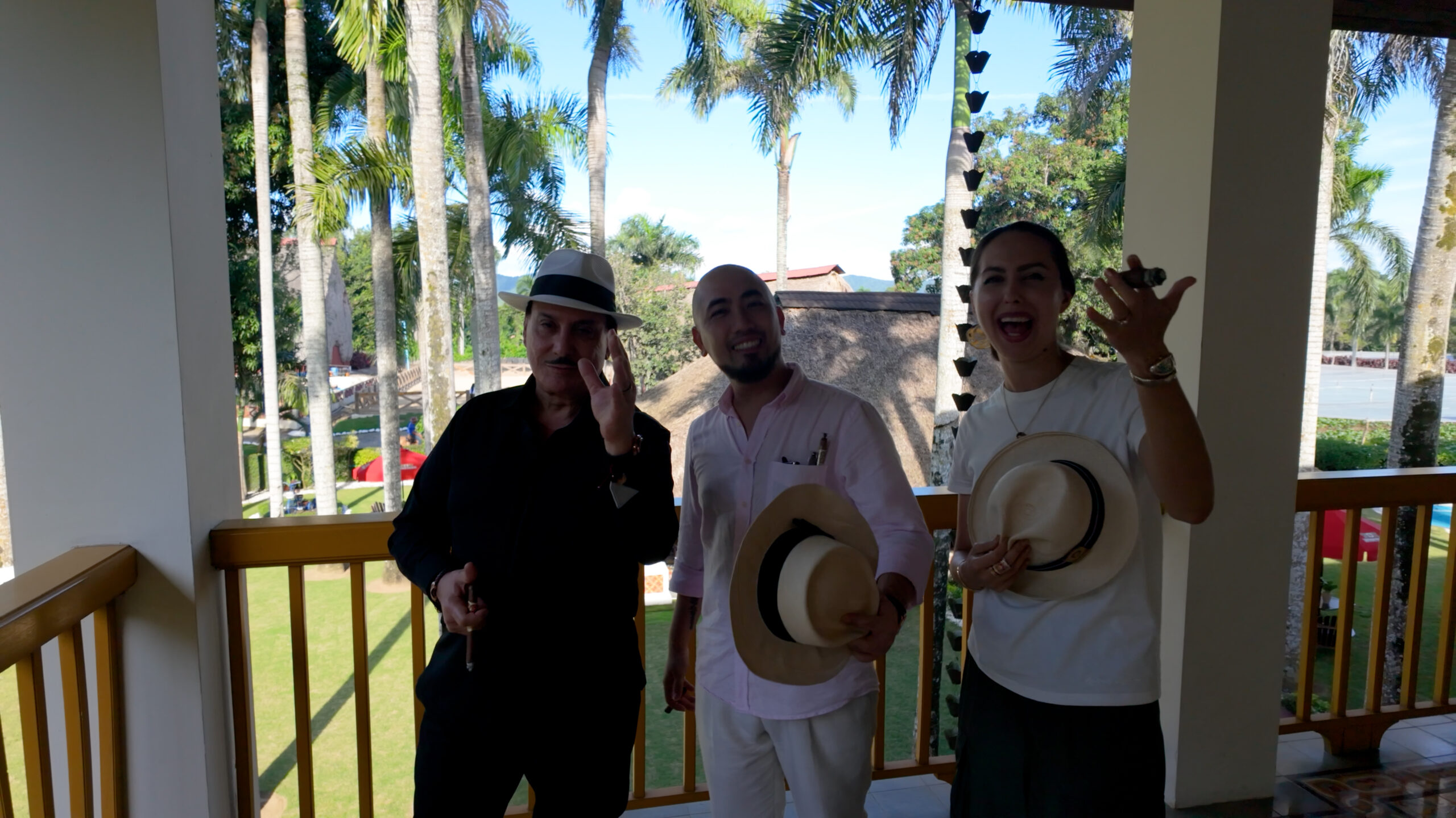 1-1-1-scaled-1 Ba người đội mũ phớt đứng trên ban công, phía sau là cảnh quan cây cọ xanh mát.