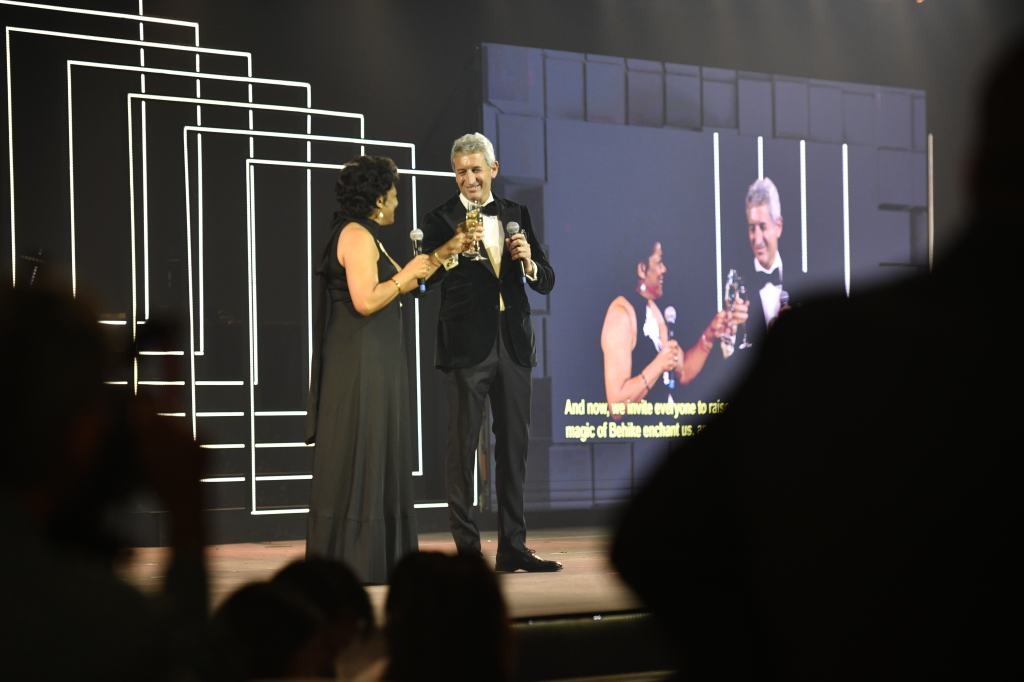 1-1-4 Hai người trên sân khấu nâng ly chúc mừng tại sự kiện nổi bật với ánh sáng sân khấu lấp lánh.