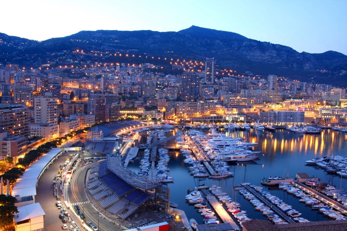 Quảng trường Monaco vào buổi tối, với bến du thuyền và thành phố rực rỡ ánh đèn.