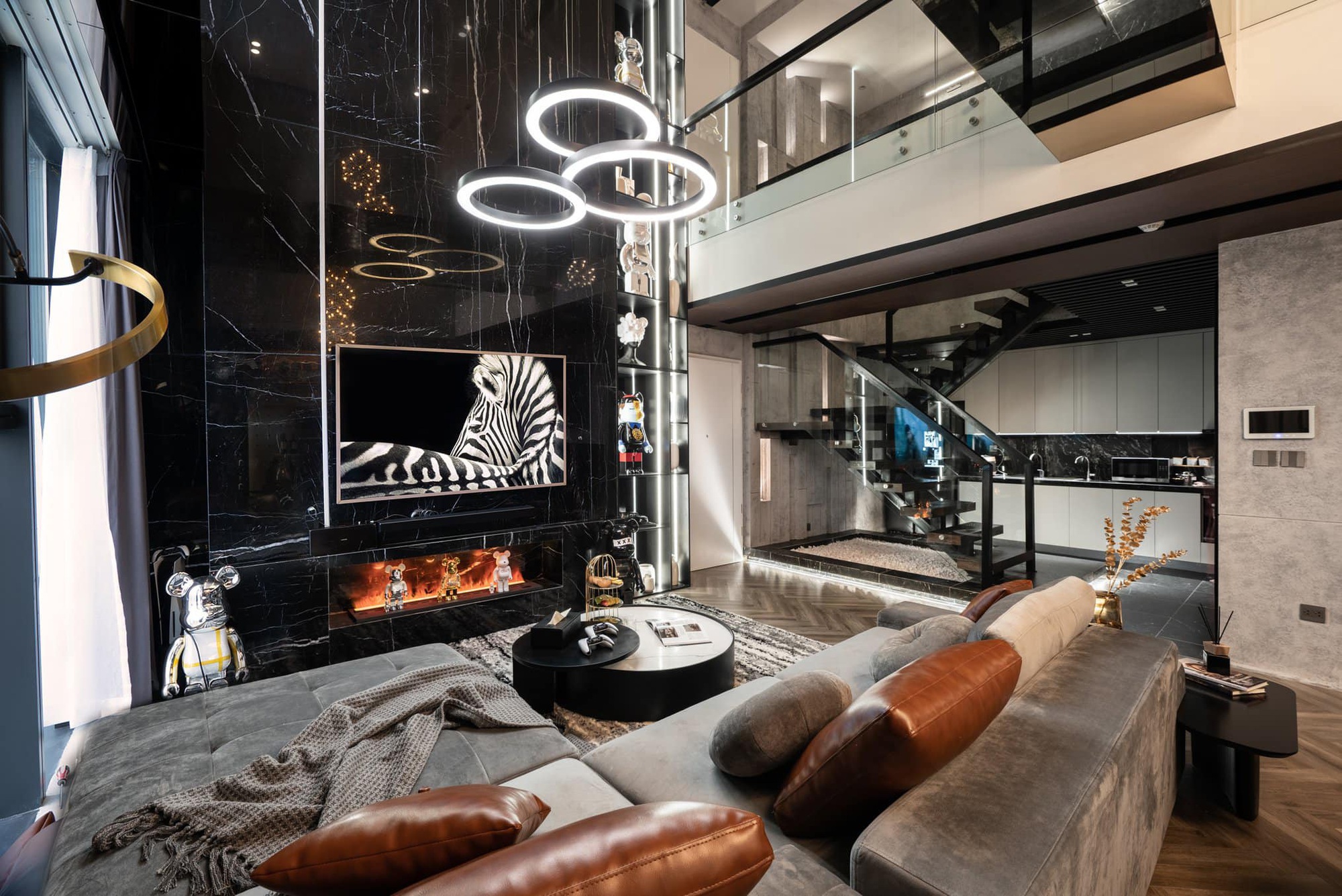Phòng khách hiện đại với sofa, đèn tròn LED, cầu thang kính và tranh vẽ ngựa vằn trên tường đá đen.