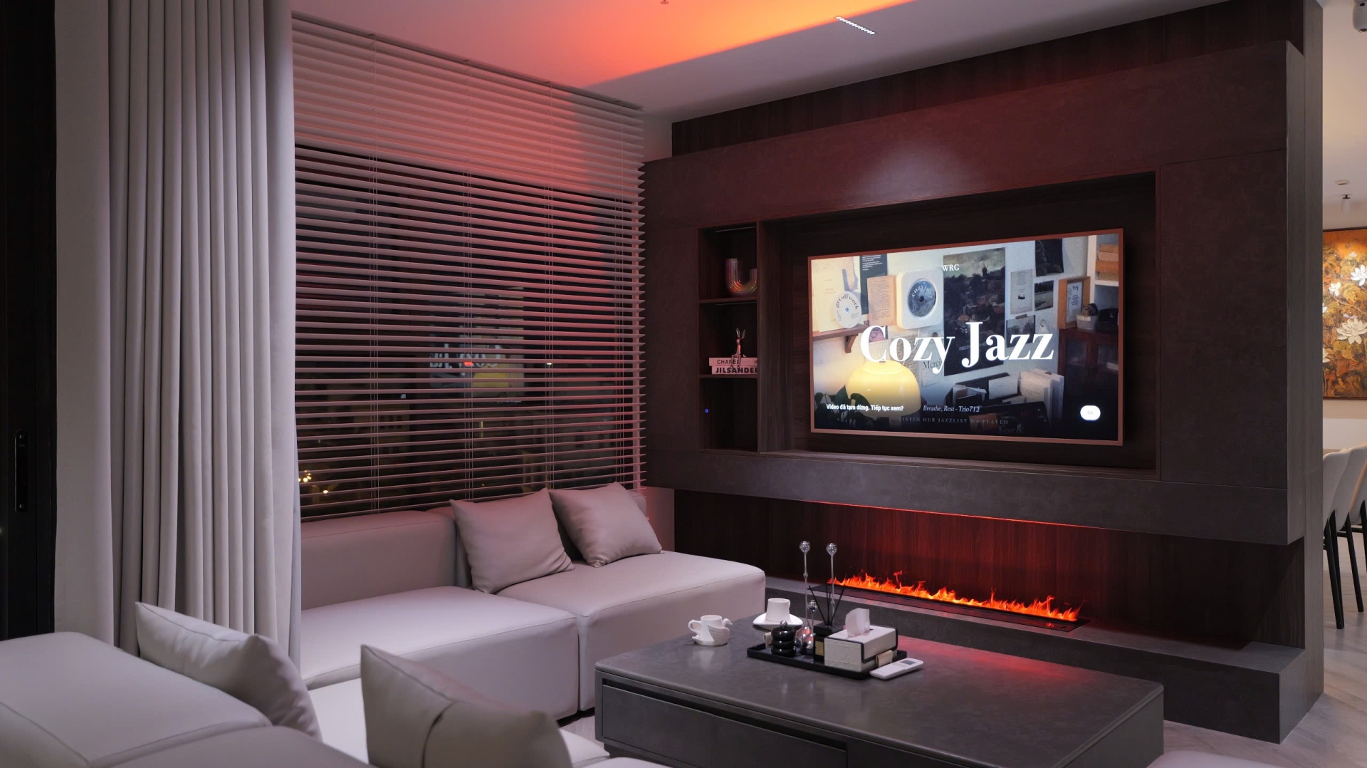Phòng khách hiện đại với sofa trắng và lò sưởi, TV hiển thị Cozy Jazz, tạo không gian thư giãn.
