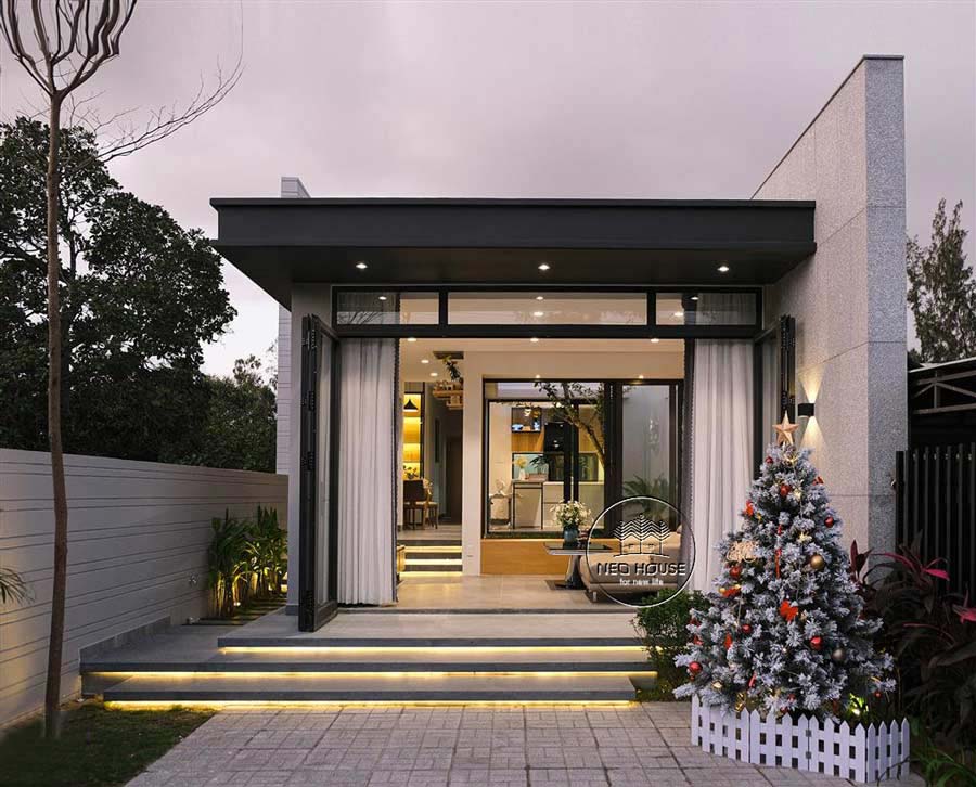 Mặt tiền ngôi nhà hiện đại được trang trí bằng cây thông Noel và ánh sáng ấm áp, với sân vườn đơn giản.