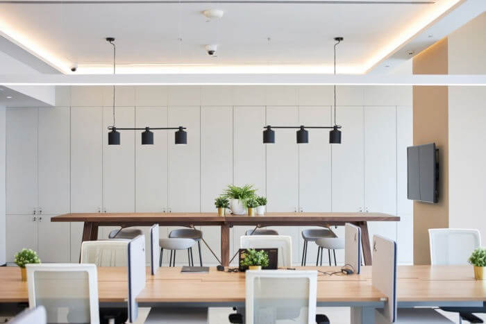 Văn phòng hiện đại với bàn gỗ dài, ghế xoay và cây xanh, ánh sáng tự nhiên tạo không gian làm việc thoải mái.