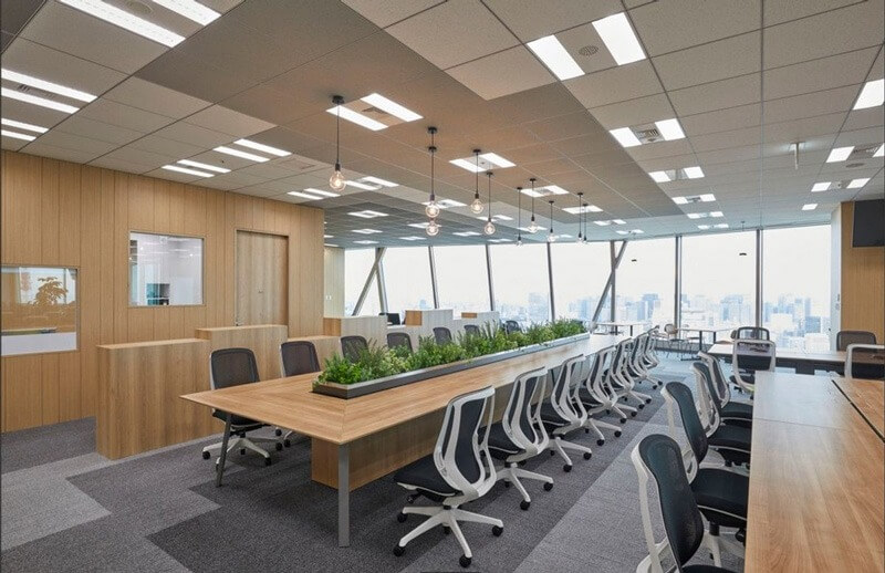Văn phòng hiện đại với bàn dài, ghế xoay và cửa sổ kính lớn nhìn ra thành phố, trang trí cây xanh.