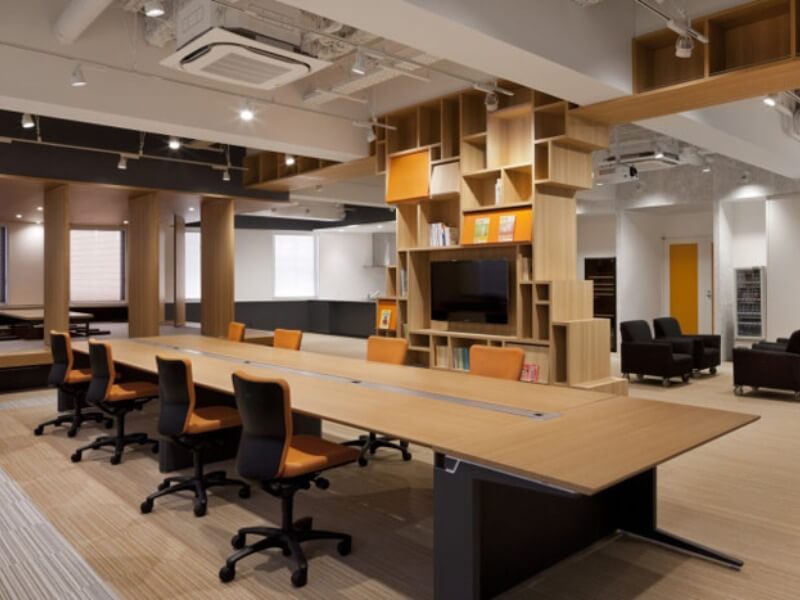 Văn phòng hiện đại với bàn gỗ dài, ghế xoay màu cam, kệ sách sáng tạo và gác lửng thoáng đãng.