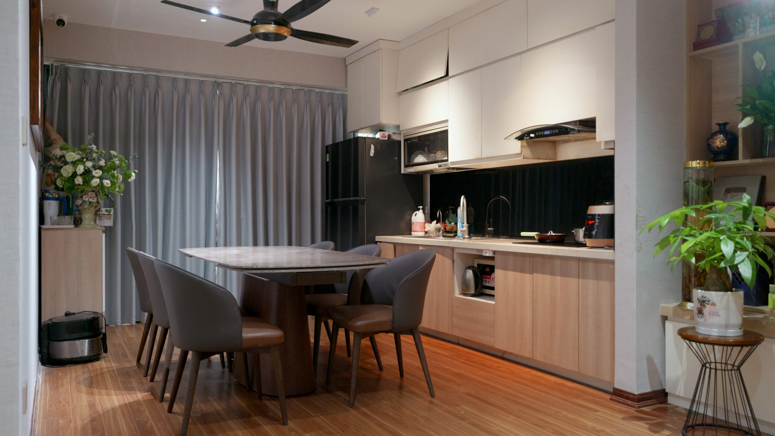 15-scaled-1-1 Nhà bếp hiện đại với bàn ăn gỗ, ghế nâu, tủ bếp trắng, và quạt trần. Cây xanh trang trí tạo điểm nhấn tự nhiên.