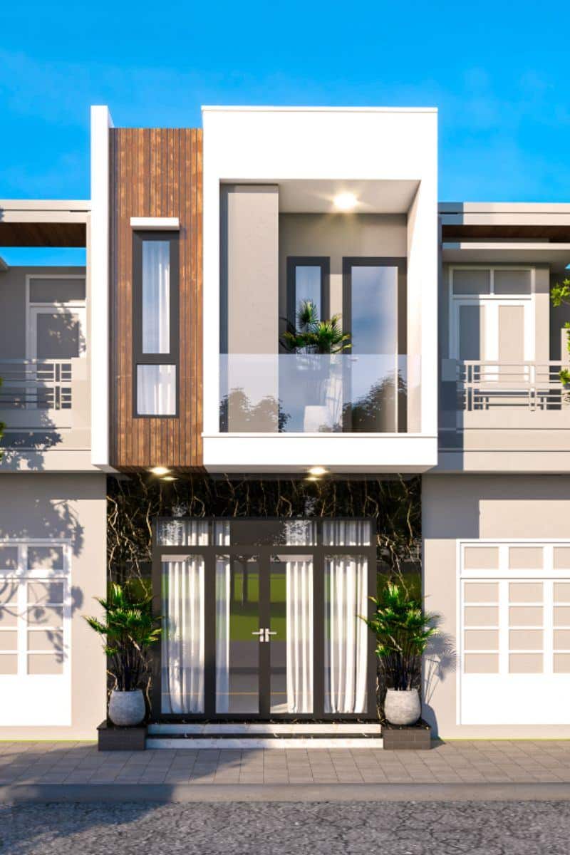 Mặt tiền nhà hiện đại nổi bật với ban công kính, cây xanh trang trí, và cửa kính lớn, lý tưởng trong môi trường đô thị.