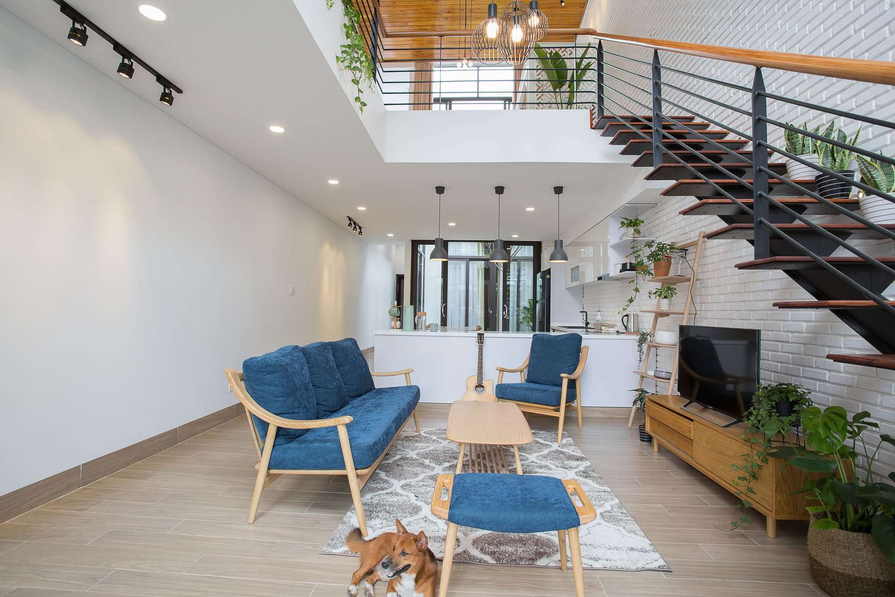 Phòng khách hiện đại với ghế sofa xanh, cầu thang gỗ và cây xanh trang trí.