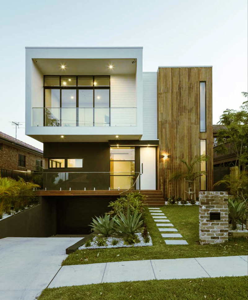 Nhà hiện đại hai tầng với mặt tiền gỗ, cửa kính lớn, và lối đi lát đá trong khu dân cư xanh.