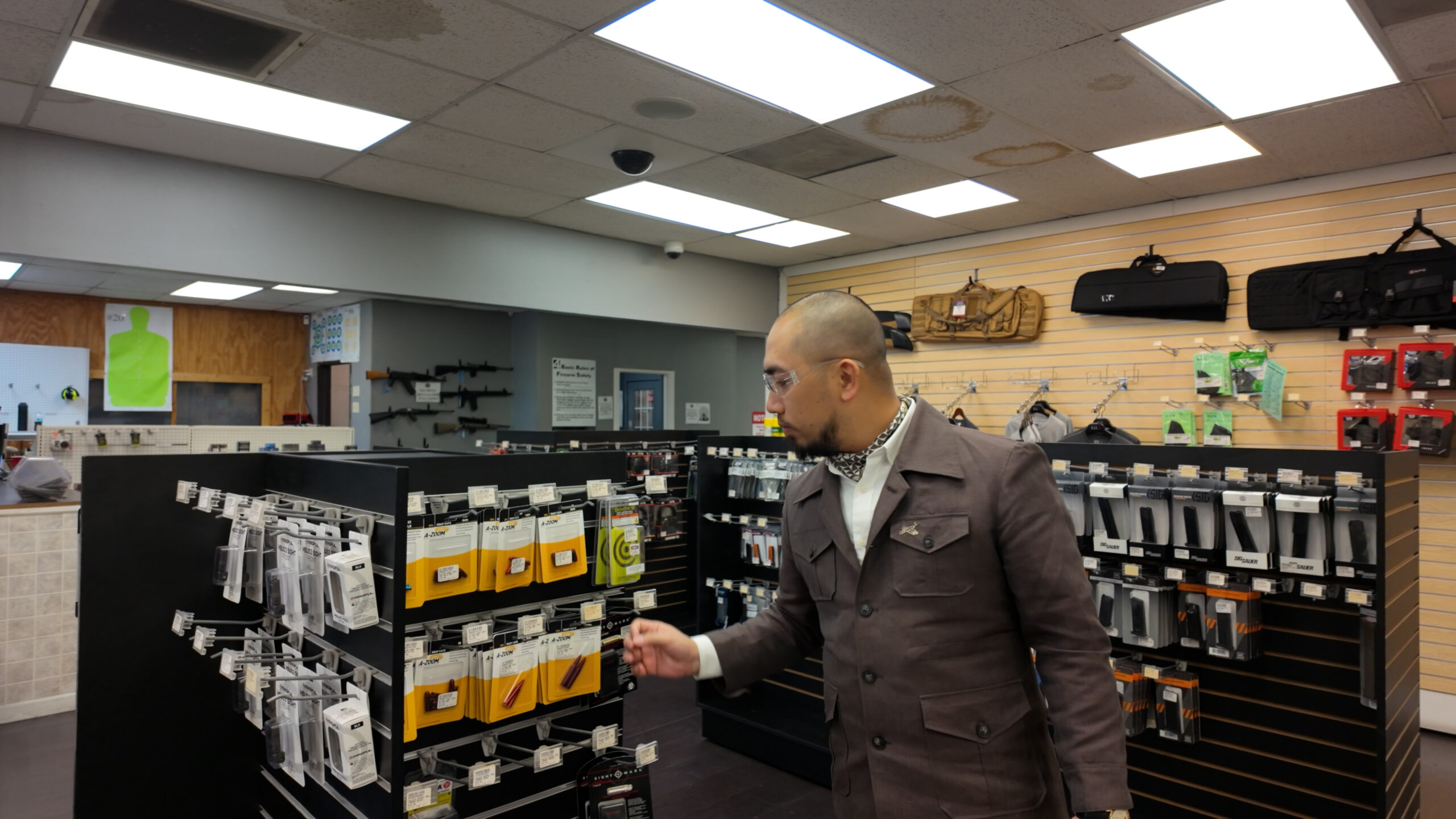 Người đàn ông xem sản phẩm trong cửa hàng bán phụ kiện bắn súng, bên trong có nhiều hàng hóa trưng bày trên kệ.