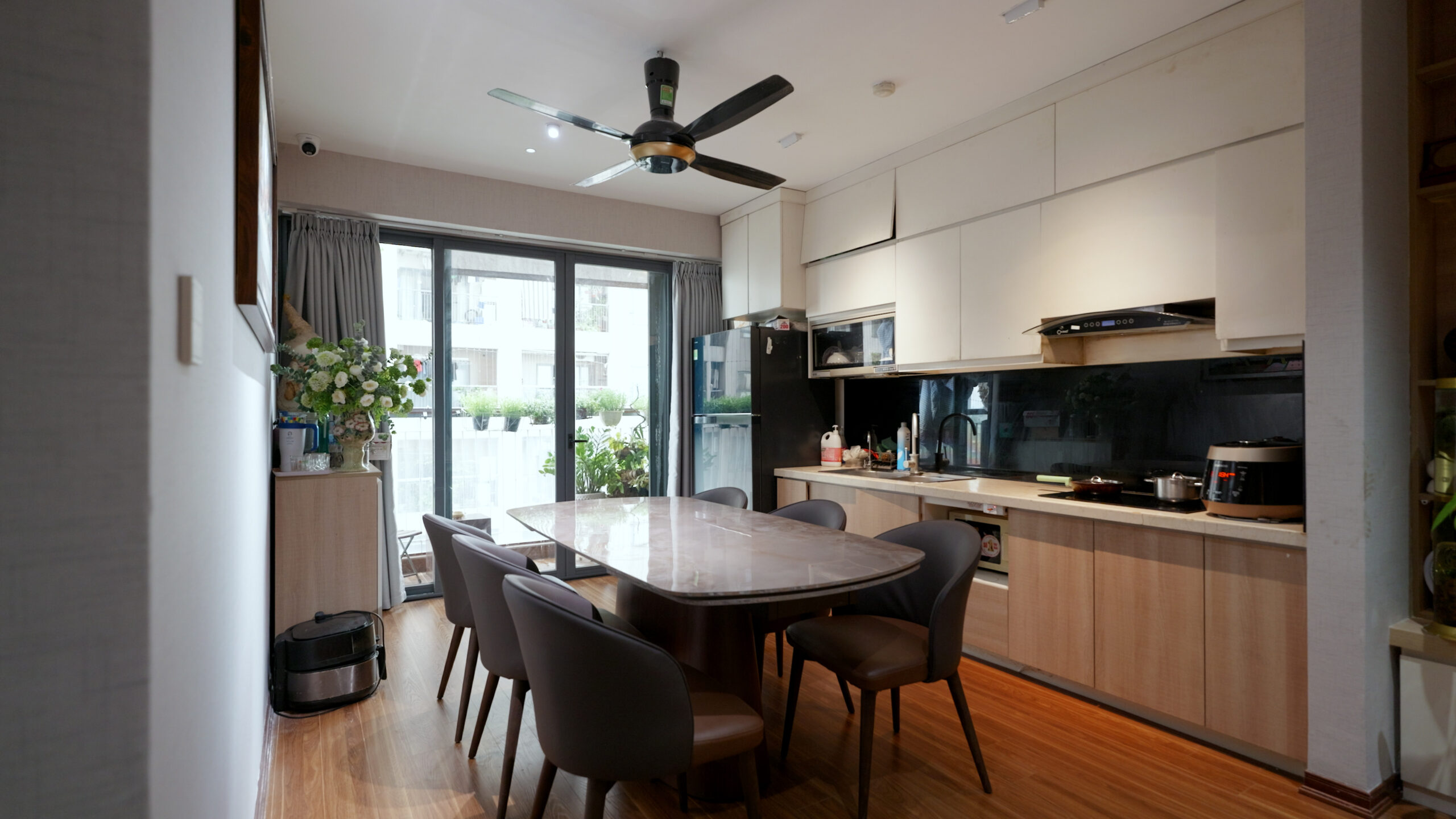 19-1-scaled-1 Nhà bếp hiện đại với bộ bàn ăn gỗ, tủ bếp trắng, quạt trần và cửa sổ lớn đón ánh sáng.
