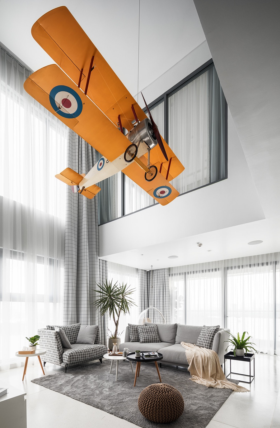Máy bay mô hình treo trong phòng khách hiện đại với sofa xám và cây xanh.