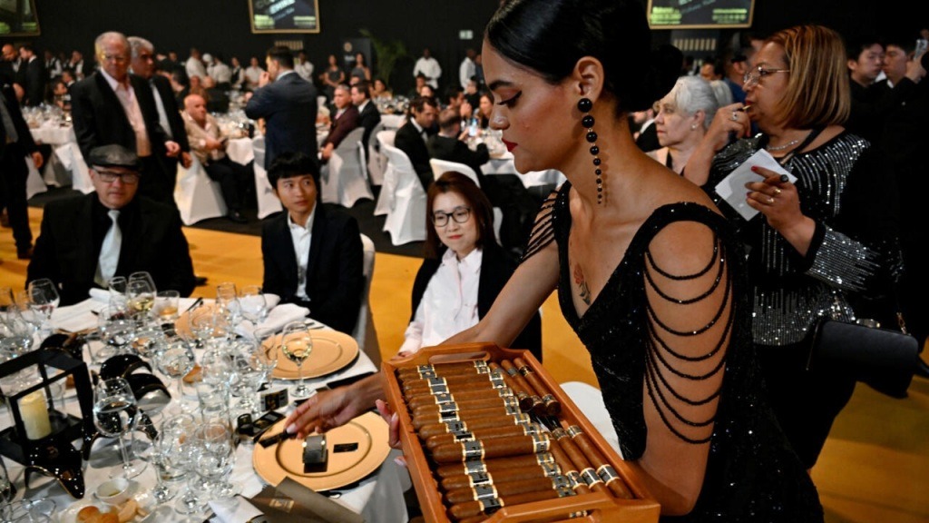 2-2-3 Người phụ nữ mặc váy đen phục vụ xì gà tại sự kiện sang trọng với bàn đầy khách dự tiệc.