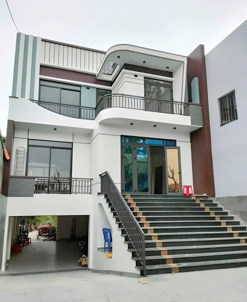 Ngôi nhà hai tầng hiện đại với cầu thang lớn và cửa kính, có ban công ở tầng hai.