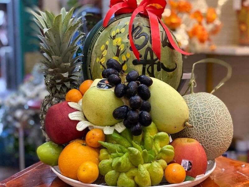 Đĩa trái cây Tết với dưa hấu, dứa, lê, nho và các loại quả khác, trang trí đẹp mắt, phù hợp mừng xuân.